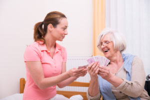 Pflegerin spielt Karten mit Seniorin
